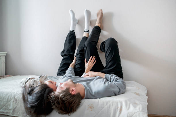istock A young couple enjoys a relaxed, affectionate moment together while lying on a bed, with their legs playfully extended upwards against a white wall. 2157740165