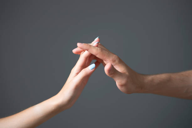 A close-up view captures the tender touch between a mans and a womans hand against a neutral gray backdrop.