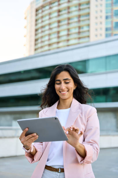 istock Smiling young middle eastern Israel businesswoman using tablet pc application for online remote work at office business building outdoors. 30s indian or arabic woman holding digital computer. Vertical 2157749294