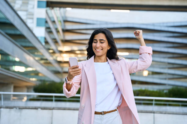istock Exiting young middle eastern Israel businesswoman winner using smartphone mobile phone financial app. Happy smiling indian arabic woman in business suit celebrating yes win gesture holding cellphone 2157749301