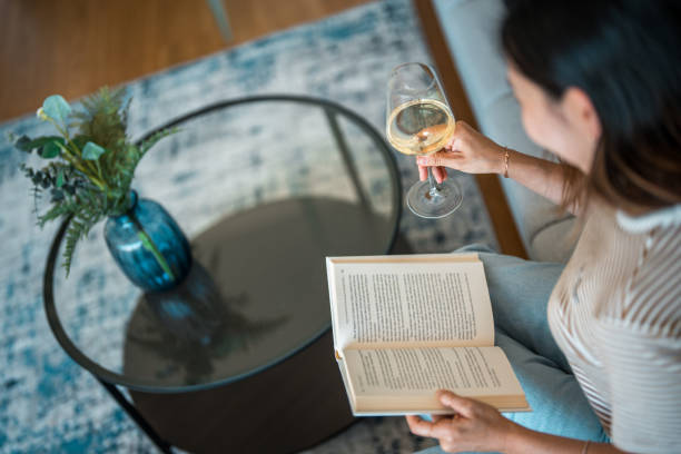 istock Woman  in Jeans Sitting  on a Sofa and Reading Novel While Drinking Wine 2157755172
