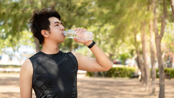 istock Asian male athlete runner drinking a water bottle in the park. Drinking refreshing drink for energy after running and outdoor exercise 2157761109