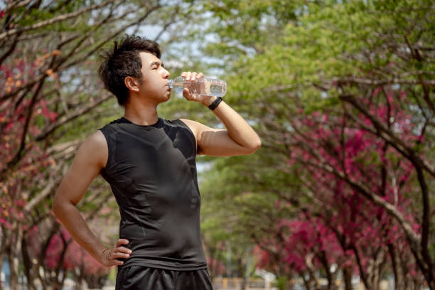 istock Asian male athlete runner drinking a water bottle in the park. Drinking refreshing drink for energy after running and outdoor exercis 2157761121