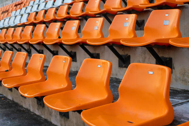 Wide view of empty plastic stadium seats arranged in neat rows, featuring bright orange chairs with a few contrasting blue ones. The repetitive pattern and vibrant colors create a modern, graphic look. Perfect for themes related to sports events, arenas, crowds, anticipation, and public venues.