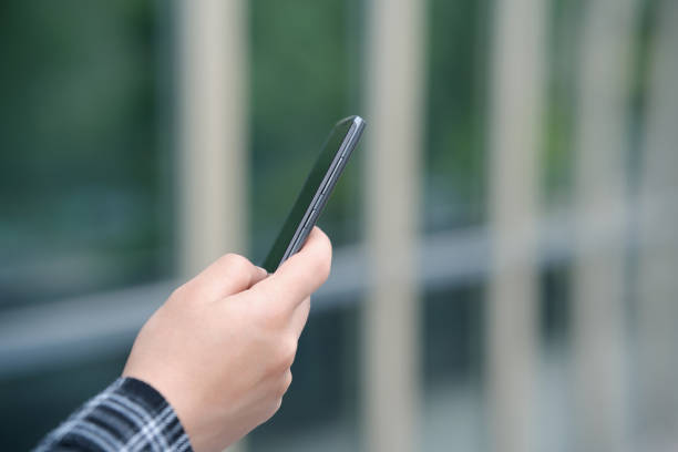 A young man's hand holding a smartphone on university campus