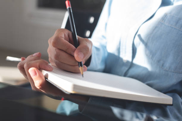 istock Woman hand with a pencil writing on paper notebook. Female student taking note on lecture chair during studying in classroom. business planning, to do list reminder 2157779454