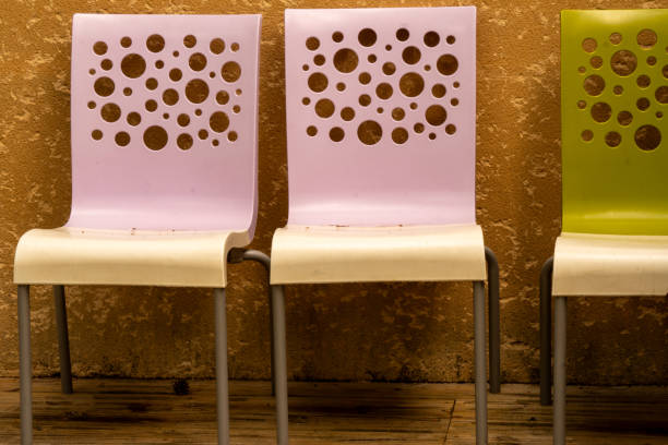 Two pink and half a green stacking chair with white seat and perforated pattern in the backrest in front of a brown house wall. Garden chairs