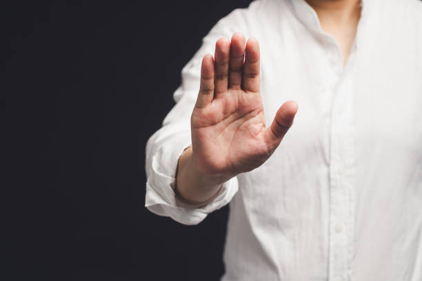 A person in a white shirt shows a stop gesture while standing on a black background. Space for text. Close-up photo.