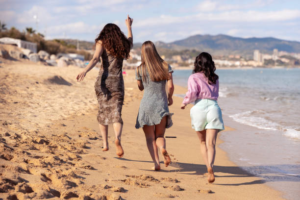 istock Rear view three female friends looking at camera on the beach having fun. 2157783713