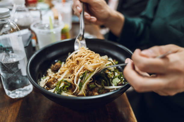 istock People eating bowls of noodles with various ingredients Using a fork and spoon This dish has noodles, vegetables, and some meat or seafood. 2157790263