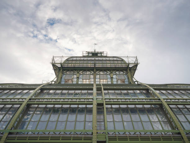 Vienna, Austria - 27 July 2023: close-up beautiful old greenhouse orangery in the park of Schönbrunn palace, founded in 1882. The view on park with buildings, trees and colorful flowers evening sunset time.