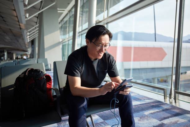 Asian male backpacker traveling alone using mobile phone to search for information online in airport waiting area