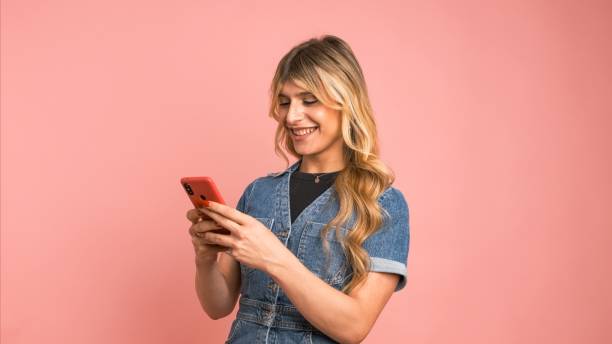 istock Happy transgender woman texting through smartphone against pink background 2157802086