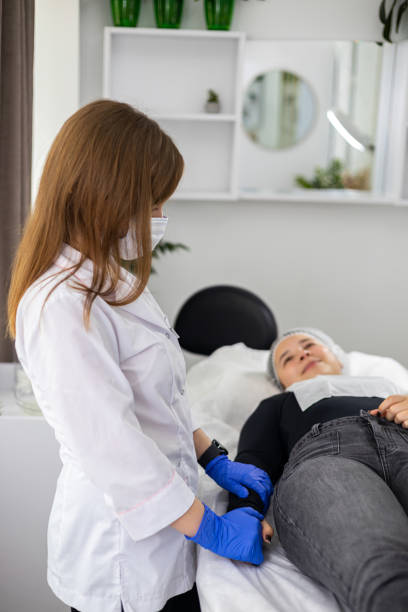 istock Beautiful young woman lying down on a procedure table and smiling while looking at the beautician which stays right near her, after a cosmetic procedure. 2157805891
