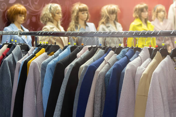 A mannequin is dressed in a white jacket and blue shirt. The mannequin is standing in a store with lights on