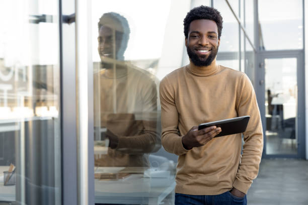 istock Positive african american guy with a tablet in hands standing outdoors 2157806476