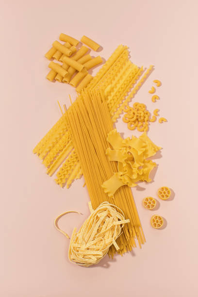 istock Assorted uncooked pasta varieties arranged on a pink background, showcasing different shapes 2157809761