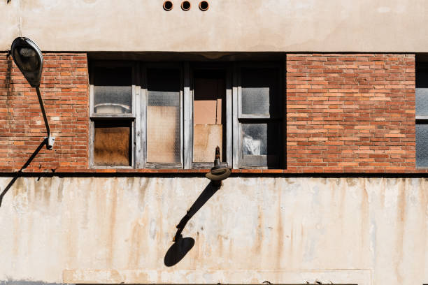 istock Urban Decay: Uneven Windows and a Lonely Lamp on a Weathered Brick Wall. The stark contrast between architectural abandonment and the resilience of time in an urban setting 2157810200