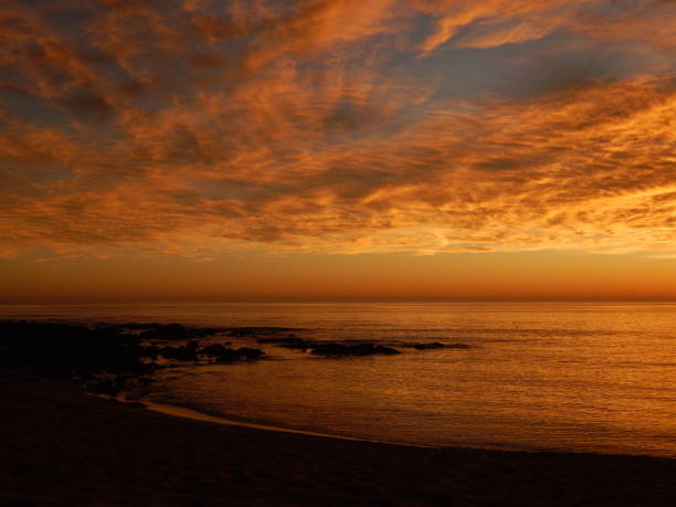 sunset over calm sea with clouds painted oragne by sunlight and rocky coastline