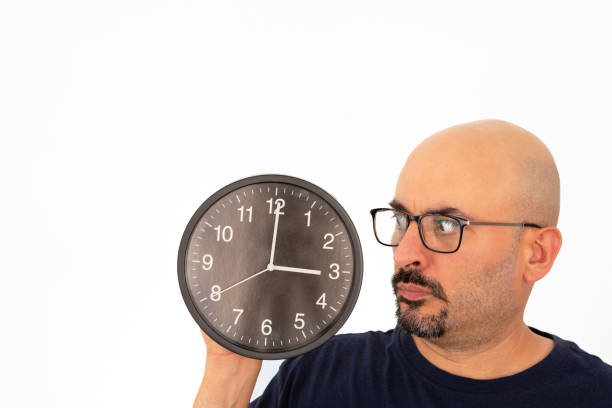 A 40-year-old man holds a large watch in his hand, examining it with a look of curiosity and intrigue. The image captures a moment of puzzled interest as he contemplates the unusual timepiece. Ideal for illustrating themes related to unique objects, curiosity, timekeeping, and the exploration of rare or peculiar items.