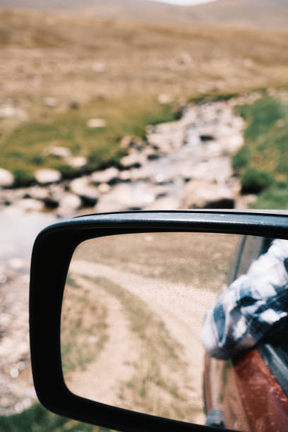 Rear-view mirror of car in mountains. Driver's elbow reflected