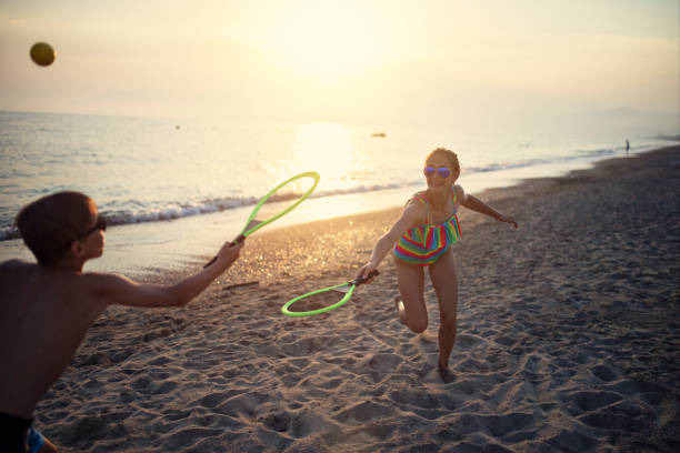 Kids having fun on the beach. Teenage girl and a little boy is playing beach tennis on sunset. \nSunny summer day evening.\nNikon D850