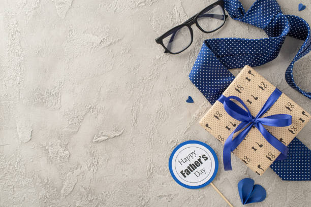istock Elevate your Father's Day tribute with charming elements: top view of sleek necktie, giftbox, glasses, postcard, and paper hearts against textured backdropâideal for heartfelt messages or promotions 2157846313