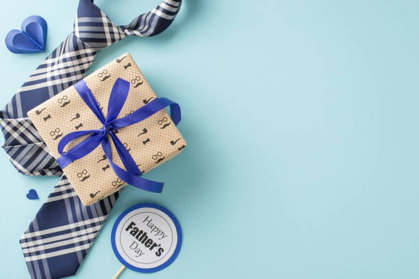 istock Personalize your Father's Day message with top view ensemble of a refined necktie, gift box, postcard on stick, and paper hearts set against a calming pastel blue background 2157846322