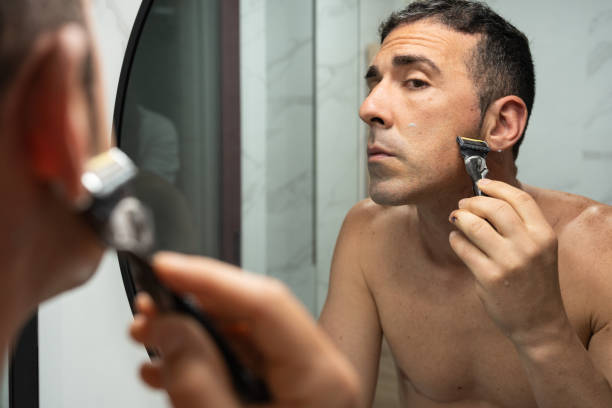 istock Young man meticulously grooms sideburns using razor's edge in bathroom mirror, emphasizing male personal care routine. Precision Shaving. 2157854884