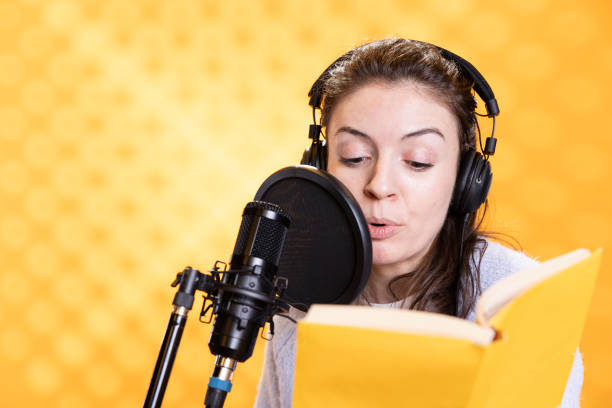 istock Woman with headphones reads aloud from book into microphone, studio background 2157867166