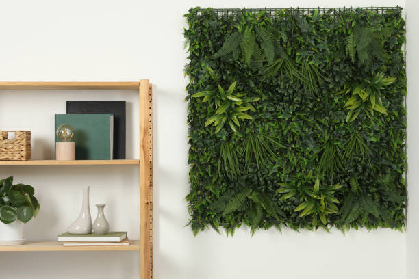 istock Green artificial plant panel on white wall and shelving unit with decorative elements in room 2157875976