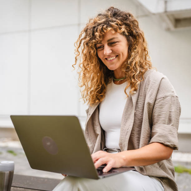 istock Adult woman sit on a bench use laptop while she have a break at work 2157878079