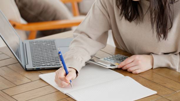 A woman calculating with a calculator and taking notes stock photo