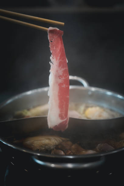 istock Man hand takes raw beef in hot pot 2157894566
