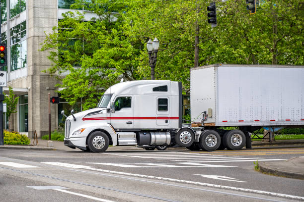 istock Powerful extended cab white big rig semi truck transporting cargo in dry van semi trailer running on the urban city street 2157899555