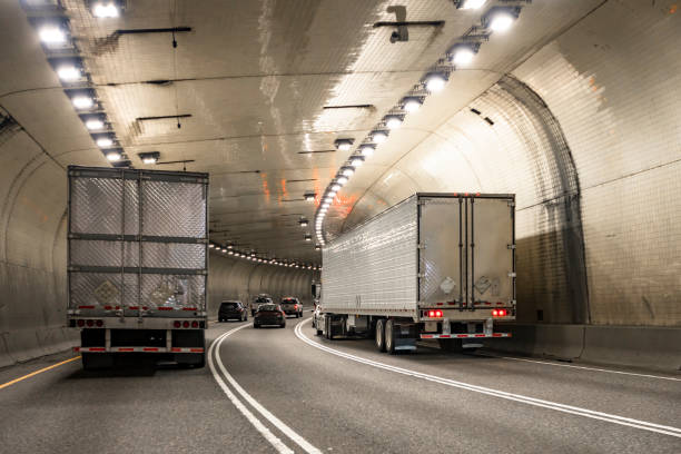 istock Professional industrial big rig semi trucks transporting cargo in refrigerated semi trailers running in long tunnel road 2157899734