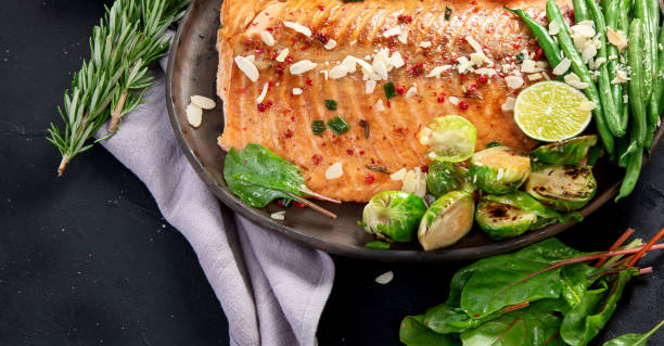 istock Cooked salmon with fresh vegetables, lime and souce. Baked fish on dark background 2157900136