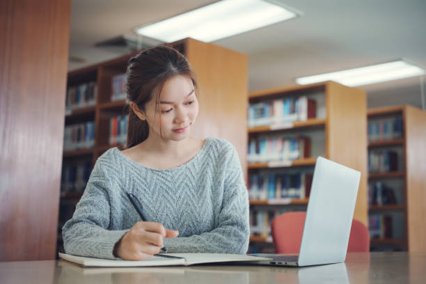 istock Asian woman student writing notes with textbooks for knowledge, information and literature project in library for research, studying and learning. 2157902370