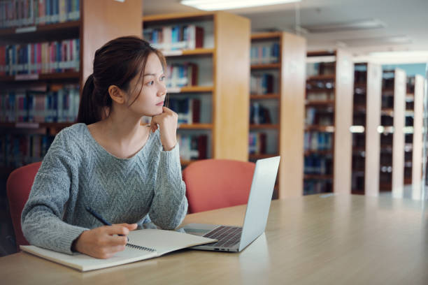 istock Asian woman student writing notes with textbooks for knowledge, information and literature project in library for research, studying and learning. 2157902371