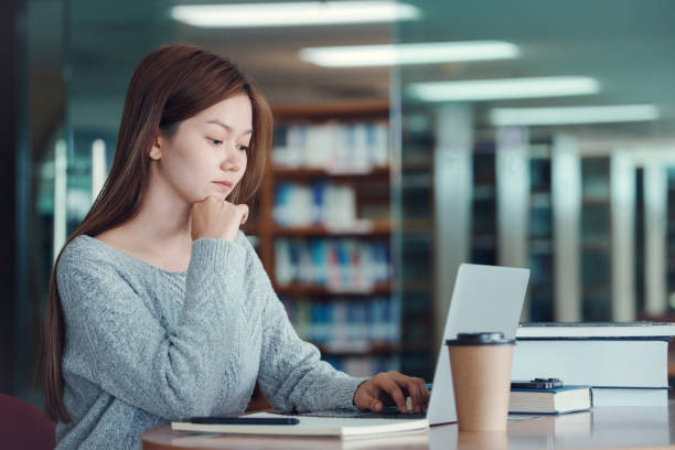 istock Asian woman student writing notes with textbooks for knowledge, information and literature project in library for research, studying and learning. 2157902539