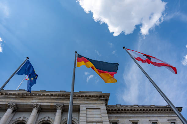 Three flags are flying on poles outside a building. The flags are of different colors and sizes, and they are all pointing in different directions. The sky is clear and blue