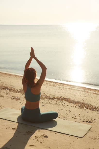 istock Woman Practicing Sunrise Yoga On Beach Facing The Ocean 2157906842