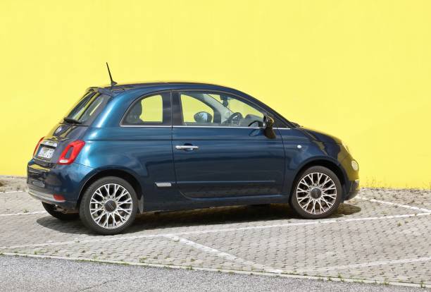 Tavagnacco, Italy. June 16, 2024. Metallic blue new Fiat 500 car on bright yellow wall background. Side view.