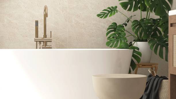istock Close up of empty brown side table by white bathtub in sunlight from window on beige marble tile wall bathroom with tropical trees 2157913295