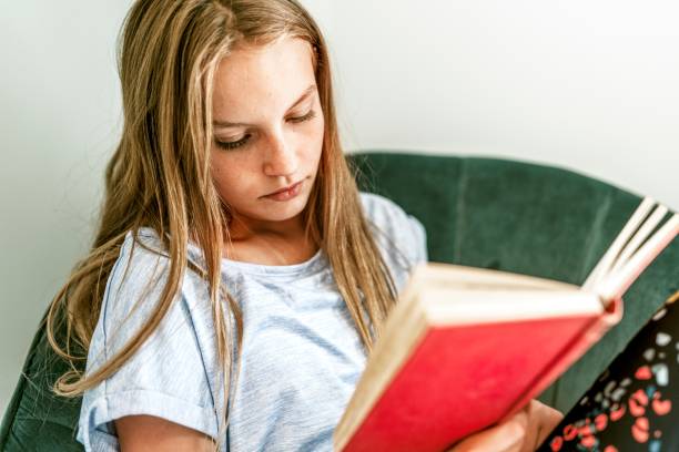 istock Young girl reading a book on a couch, new normal hobby 2157914663