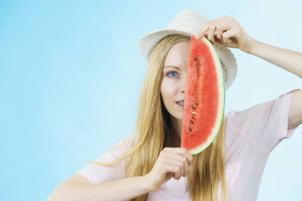 Happy cheerful teenage girl ready for summer wearing sun hat holding sweet fruit red juicy watermelon, on blue