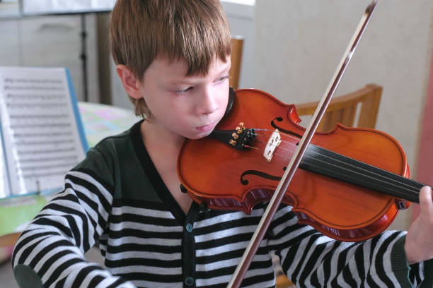 istock Boy of 8 years is playing violin using notes at home. 2157924817