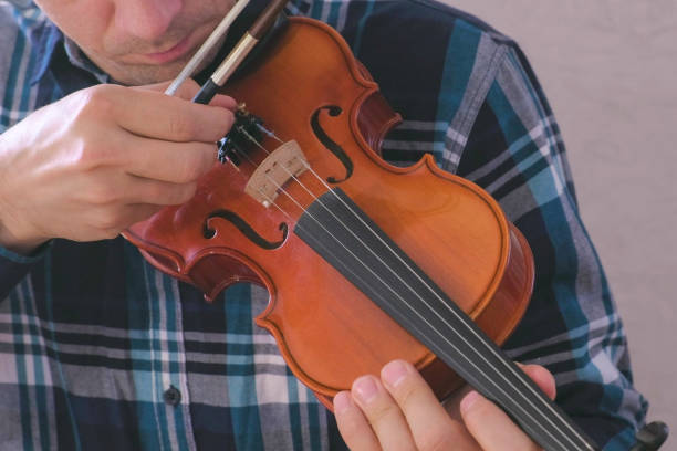 istock Man adjusts the violin twisting the bolts and playing it with a bow. 2157924827