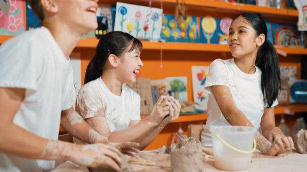istock Girl modeling cup of clay while looking at smart boy at art class. Edification. 2157929354