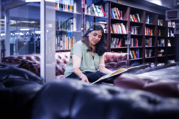 istock Quiet evening read. Hispanic woman engrossed in large book at library. 2157929484